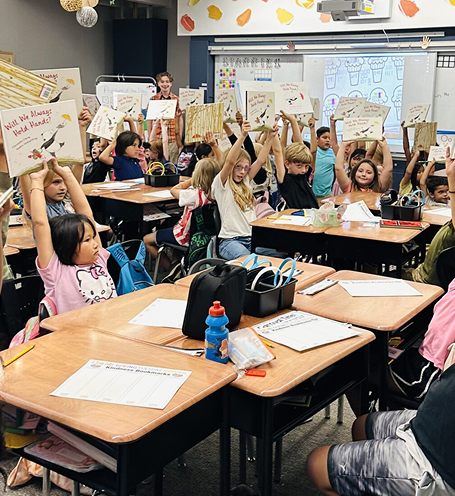 Students raising books in a classroom